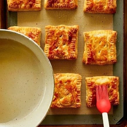 Brushing baked pastelitos with sugar glaze